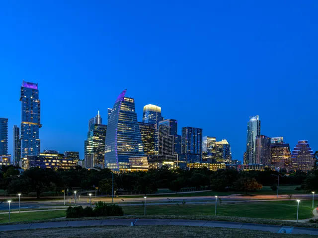Austin’s illuminated skyline rises above the dark park grounds beneath a clear blue evening sky.