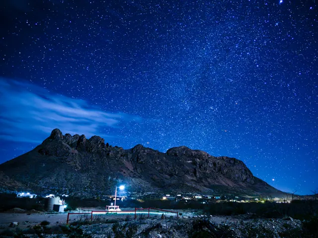 Stars fill a deep blue sky above the Christmas Mountains near Terlingua, with scattered lights below.