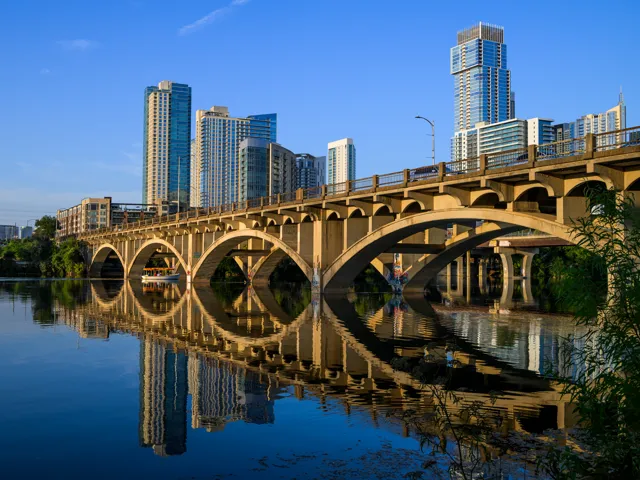 The arches of Lamar Boulevard Bridge and the Austin skyline reflect in Lady Bird Lake.