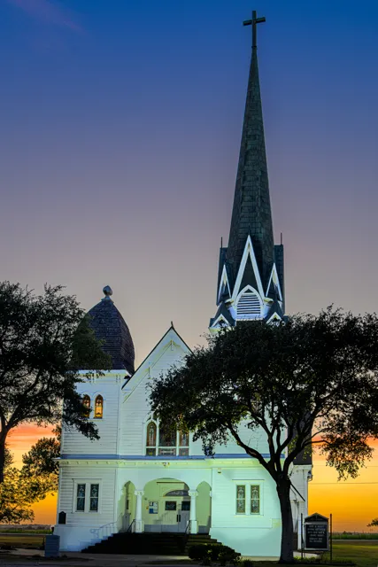 The slender steeple of New Sweden Lutheran Church rises into the evening sky above its white facade.