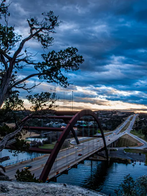 Trees frame Pennybacker Bridge and Lake Austin as the last light gathers along the horizon.