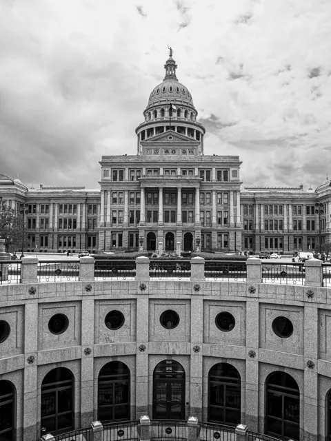The Texas Capitol appears beyond the curved walls of the reverse rotunda in black and white.